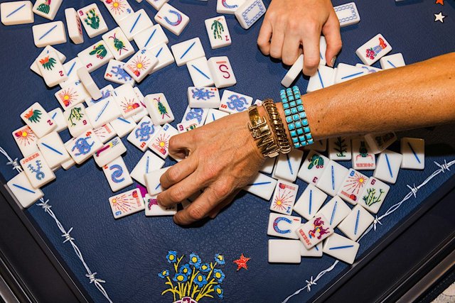 Hands sorting white mahjong tiles with joker, cactus and sunburst designs across a navy blue game table