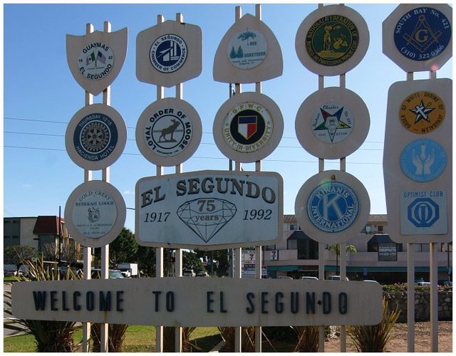 The Welcome to El Segundo sign surrounded by civic club emblems under a blue sky