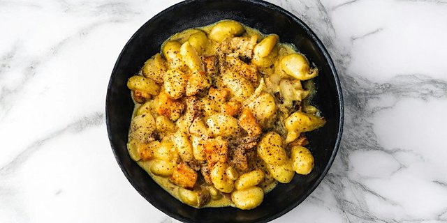Bowl of golden gnocchi with roasted squash in a creamy sauce on a marble surface