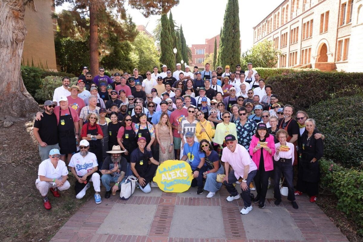 Large group of chefs and volunteers in aprons posing on a brick path at UCLA behind an L.A. Loves Alex's Lemonade sign