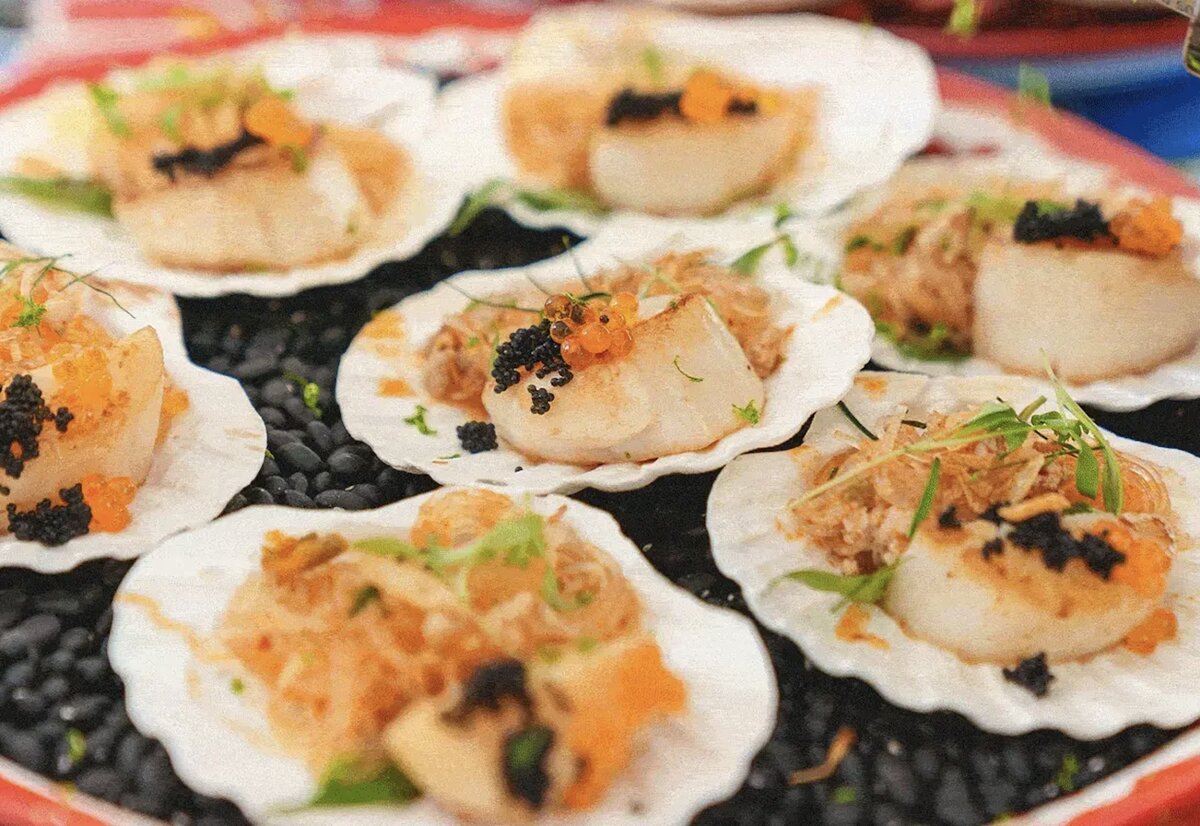 Seared scallops topped with caviar and roe served in shells on a bed of black stones