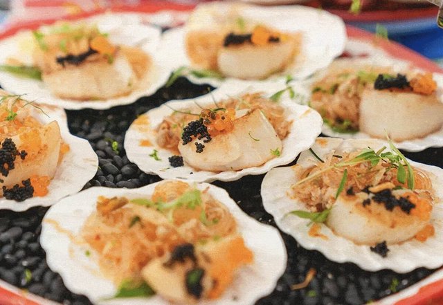 Seared scallops topped with caviar and roe served in shells on a bed of black stones
