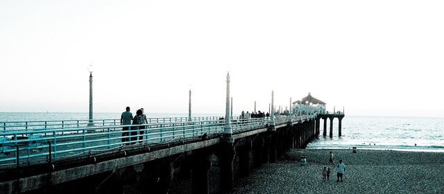 Visitors stroll the Manhattan Beach Pier at dusk, with the round building at its end over the Pacific