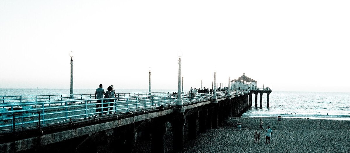 Visitors stroll the Manhattan Beach Pier at dusk, with the round building at its end over the Pacific
