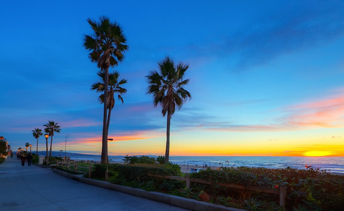 Palm trees and a lamp-lit walkway beside the beach in Manhattan Beach at sunset