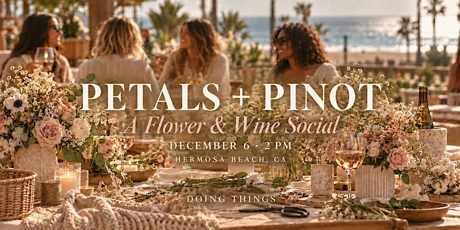 Long table set with flower arrangements, wine glasses and candles, with guests seated in front of a beach view
