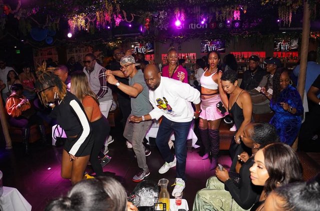 Guests dancing and mingling among tables under purple lighting and hanging greenery inside Jungle Hollywood