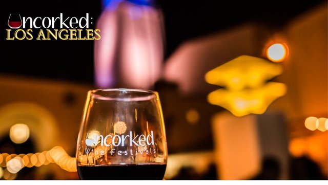 Stemmed wine glass etched with the Uncorked Wine Festivals logo against warm blurred lights at night