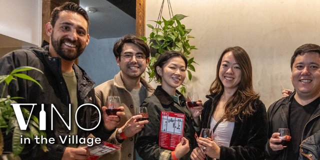 Five smiling friends holding glasses of red wine and a tasting map at Vino in the Village
