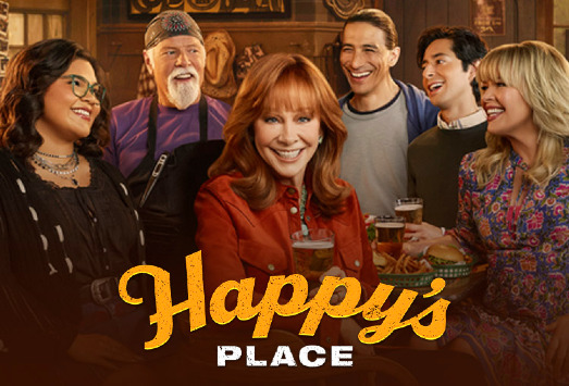 Reba McEntire in a rust-colored jacket smiles at a bar table surrounded by the Happy's Place cast, with the show's gold script logo across the bottom
