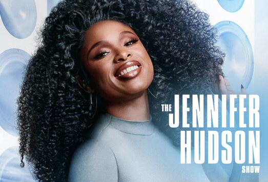 Jennifer Hudson smiling with voluminous curly hair in a pale blue top, beside The Jennifer Hudson Show title lettering