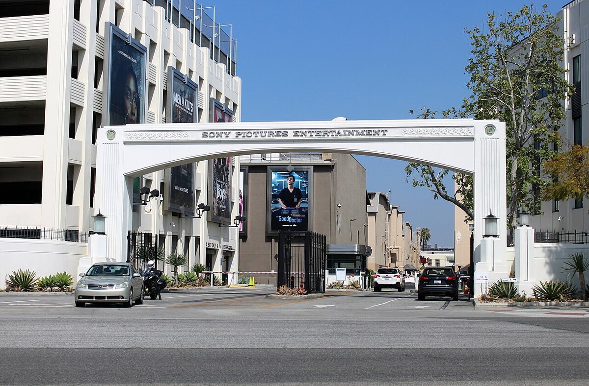 The white Sony Pictures Entertainment arch over the studio entrance in Culver City, with cars waiting at the gate and billboards on the buildings behind