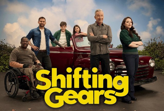 Shifting Gears cast posed around a deep red vintage pickup truck under a cloudy blue sky, with Tim Allen and Kat Dennings standing arms crossed beside the yellow show title