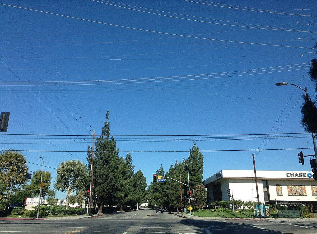Wide Northridge intersection under a blue sky, with power lines overhead and tall trees along the street