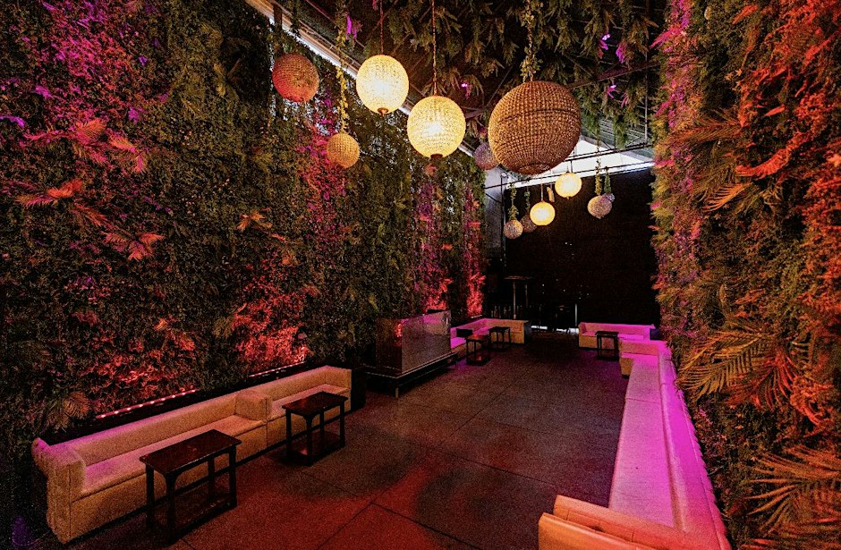 Lounge room with pink-lit living plant walls, woven globe lanterns hanging overhead and white banquettes around low tables