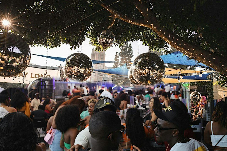 Crowd mingling under hanging disco balls and string lights at an outdoor day party