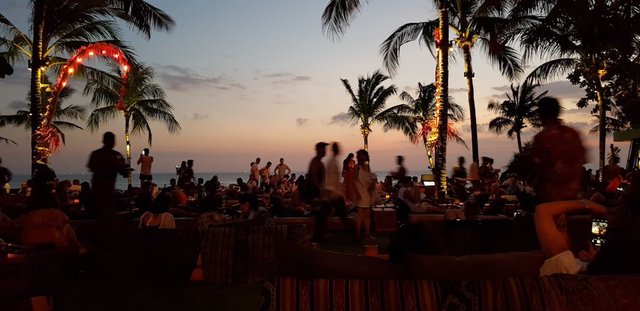 A group of people gathered at an outdoor gathering near a beach at sunset