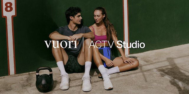 A man and a woman in athletic wear sit against a green wall beside a kettlebell, with the Vuori ACTV Studio logo between them