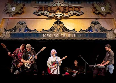 The gilded proscenium of The Belasco, with the theatre's name and 1050 South Hill lettered above a band playing on the stage