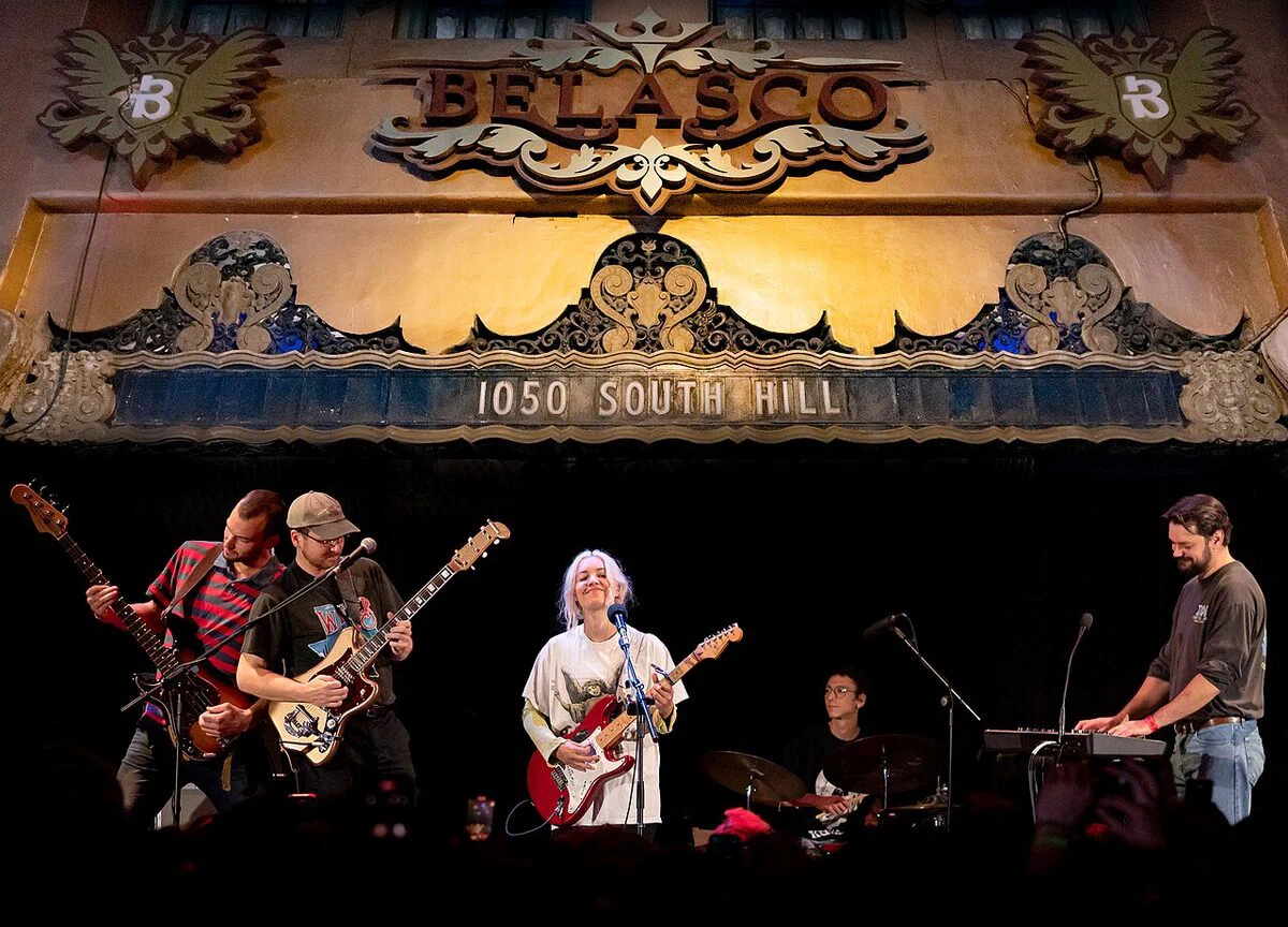 The gilded proscenium of The Belasco, with the theatre's name and 1050 South Hill lettered above a band playing on the stage