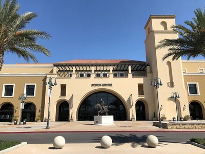 The tan Mission-style main entrance of the Fowler Events Center in Riverside, with its arched doorway, bell tower and palm trees under a clear blue sky