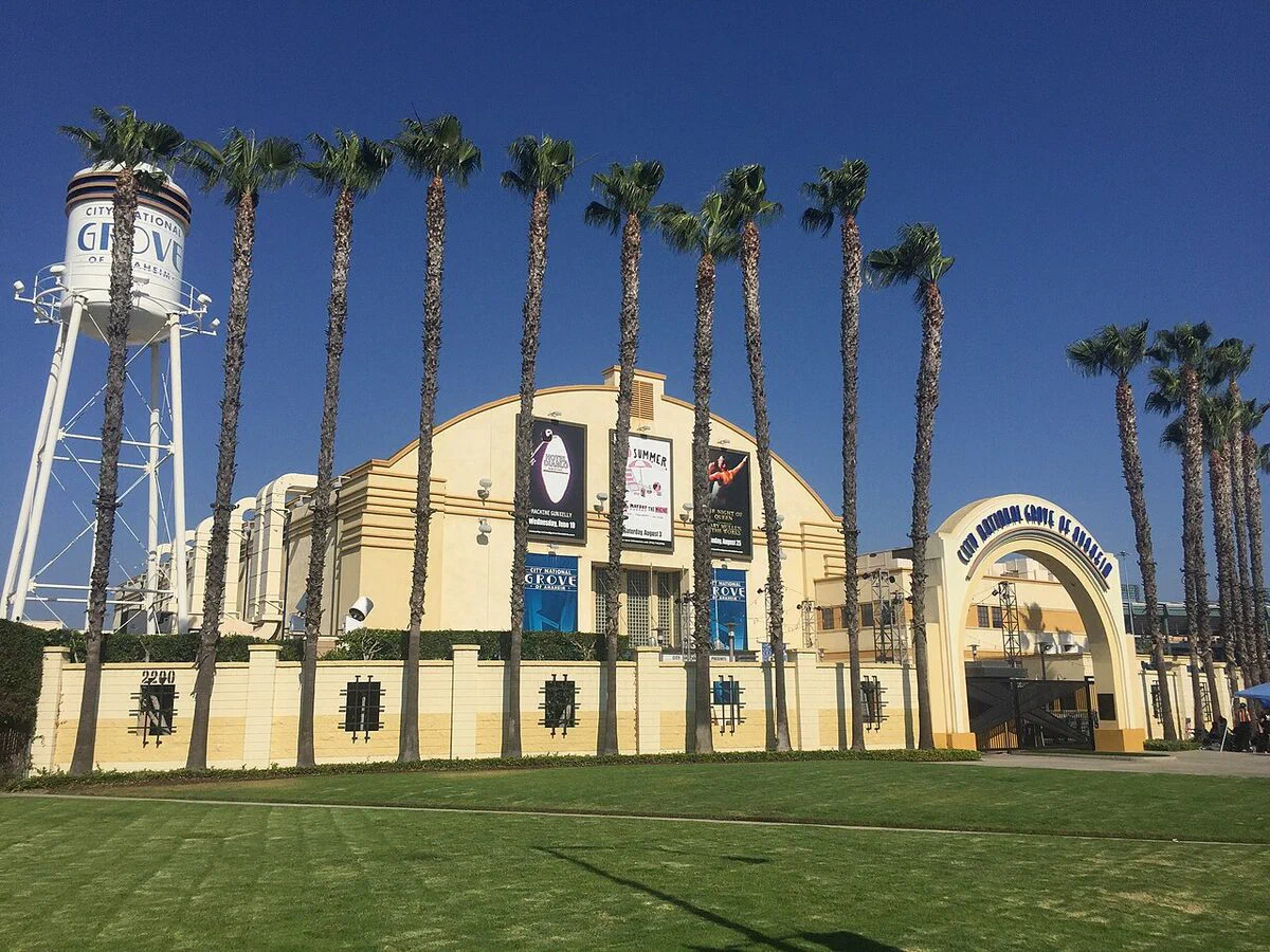 The cream-colored arched facade, palm trees and water tower of the DigAlert Grove of Anaheim, shown under its earlier City National Grove signage