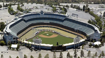 Aerial view of Dodger Stadium's tiered stands and green field, ringed by palm trees and empty parking lots in Chavez Ravine