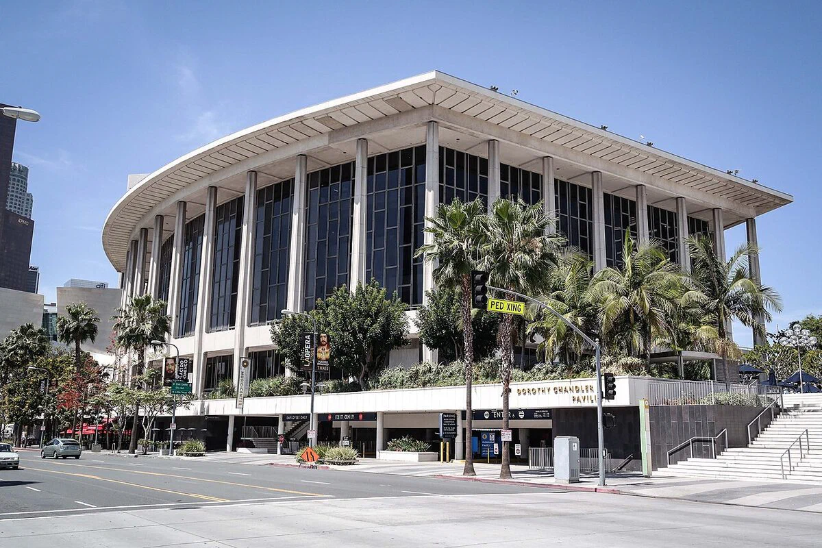 The Dorothy Chandler Pavilion's white columns and curved roofline above Grand Avenue on a clear day, with its name sign on the street-level wall
