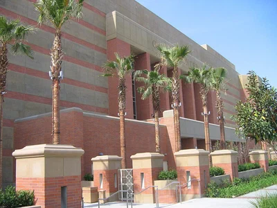 Galen Center's red brick and tan facade behind a row of palm trees on the USC campus in Los Angeles