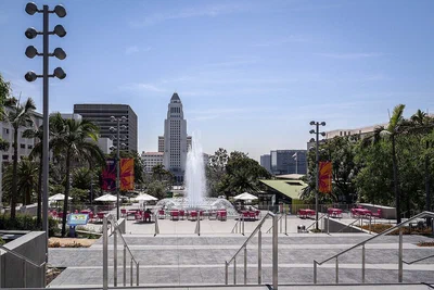 Los Angeles City Hall rising behind the fountain plaza, palm trees and pink chairs of Grand Park on a clear day