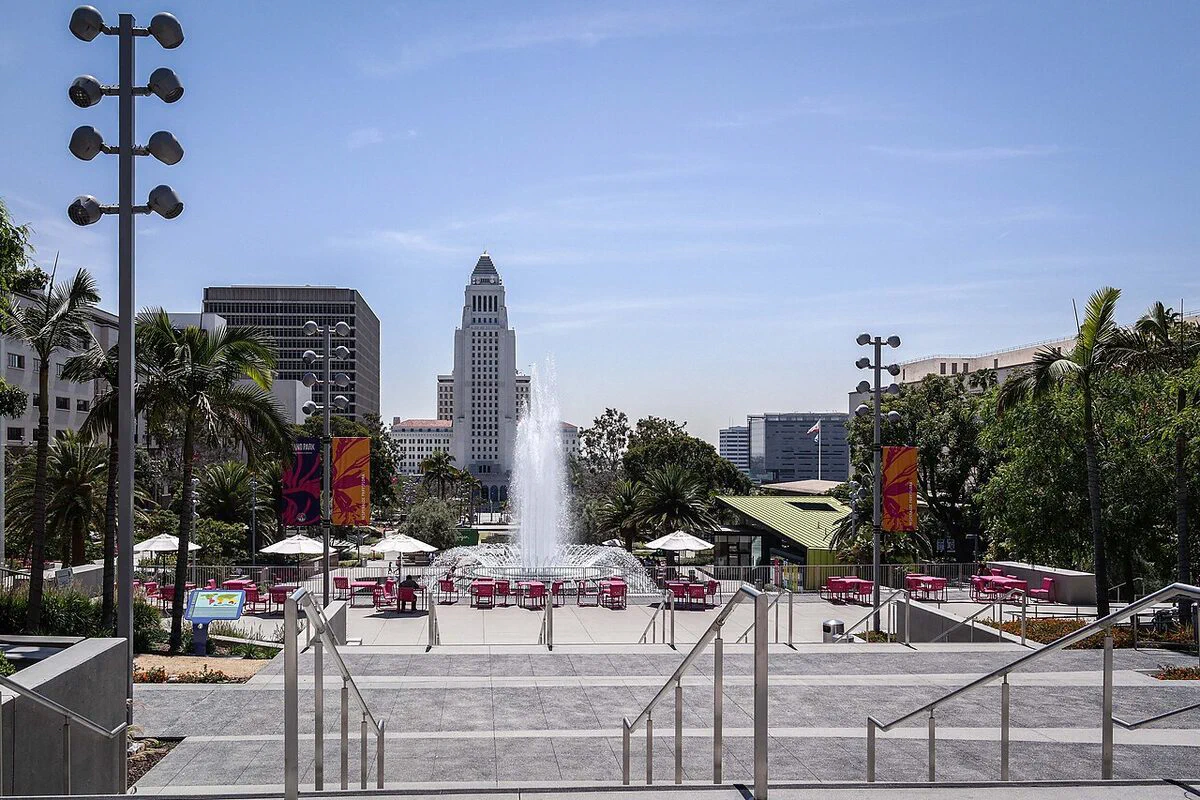 Los Angeles City Hall rising behind the fountain plaza, palm trees and pink chairs of Grand Park on a clear day