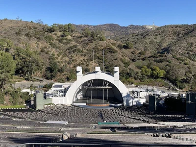 The Hollywood Bowl's white band shell and rows of empty seats in daylight, with the Hollywood Hills and the Hollywood sign behind