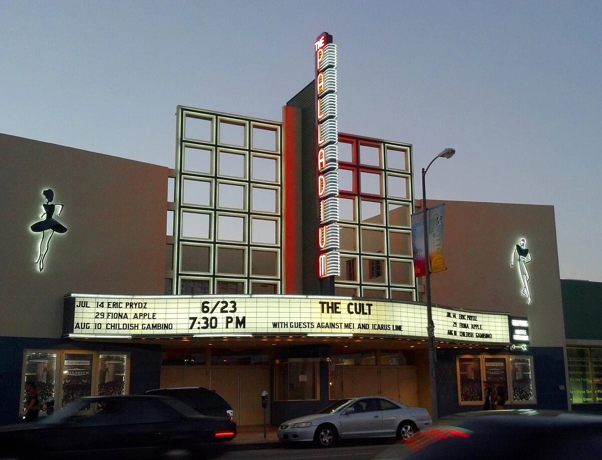 The Hollywood Palladium's vertical PALLADIUM sign and glass-fronted tower above the marquee on Sunset Boulevard at dusk