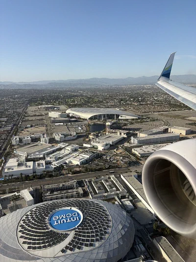 The round roof of Intuit Dome with its logo, seen from a plane window over Inglewood with SoFi Stadium in the distance