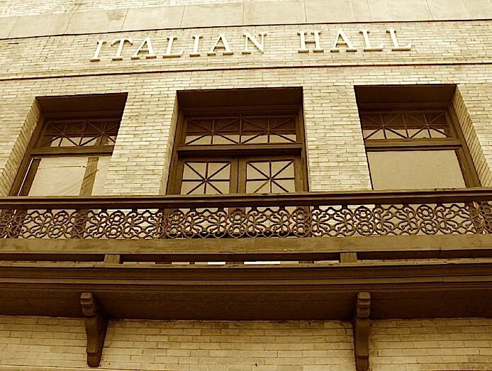 The brick front of the Italian Hall, home of the Italian American Museum of Los Angeles, with the hall's name lettered above a wrought iron balcony