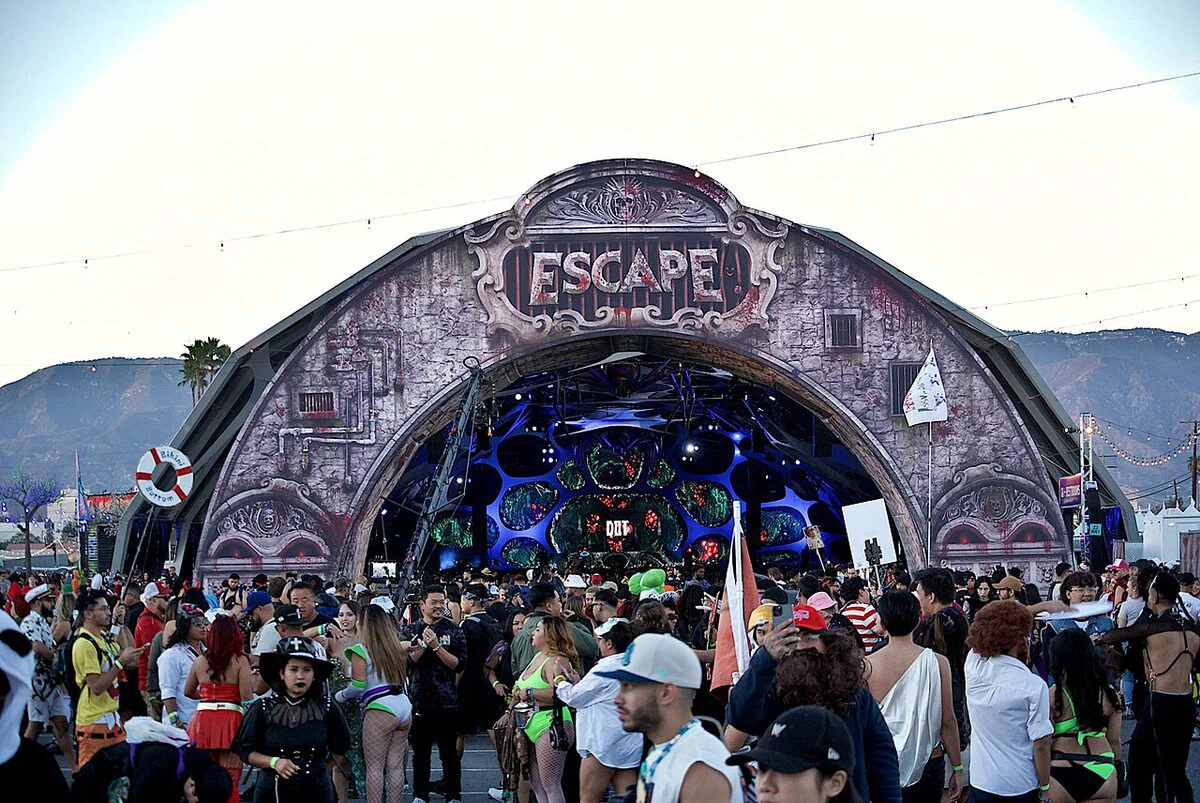 The Escape festival's ornate main stage arch at dusk on the NOS Events Center grounds, with a costumed crowd in front and mountains behind