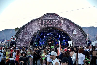 The Escape festival's ornate main stage arch at dusk on the NOS Events Center grounds, with a costumed crowd in front and mountains behind