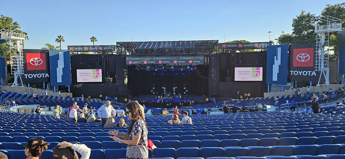 Rows of blue seats facing the covered stage and video screens at Pacific Amphitheatre on a sunny afternoon before a show
