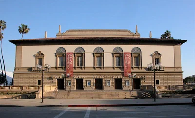 The Pasadena Civic Auditorium's cream facade with arched windows, red banners and a tiled roofline on Green Street under a blue sky