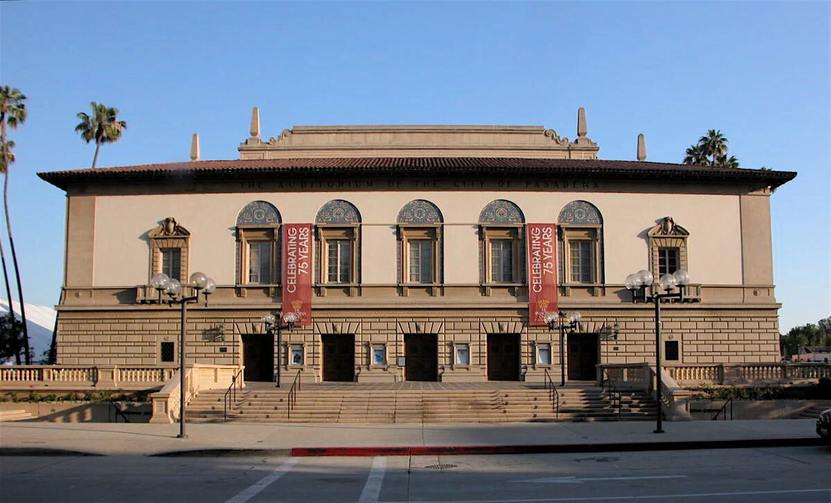 The Pasadena Civic Auditorium's cream facade with arched windows, red banners and a tiled roofline on Green Street under a blue sky