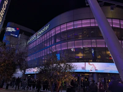 The curved glass front of Peacock Theater lit purple at night at L.A. Live, with its name across the top and a line of people outside