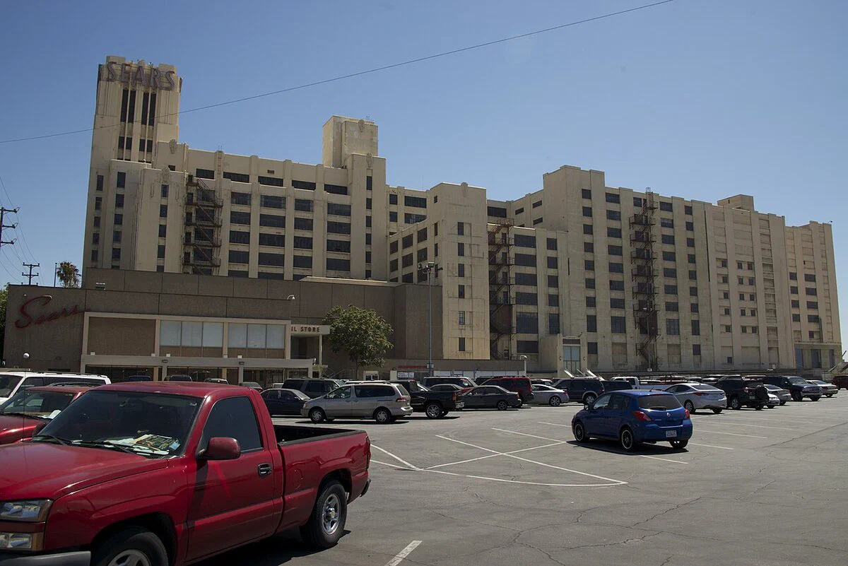 The Historic Sears Building and its rooftop Sears sign seen across a parking lot in Boyle Heights, the backdrop of the Rio Vista Lot at The Historic Sears Building