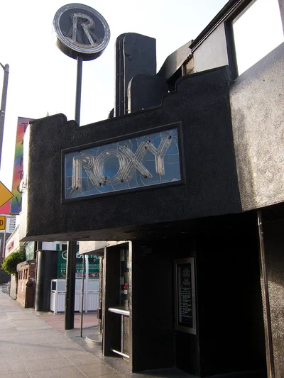 The Roxy's black stucco front on Sunset Boulevard with its lit ROXY sign and the round R sign on a pole above the entrance