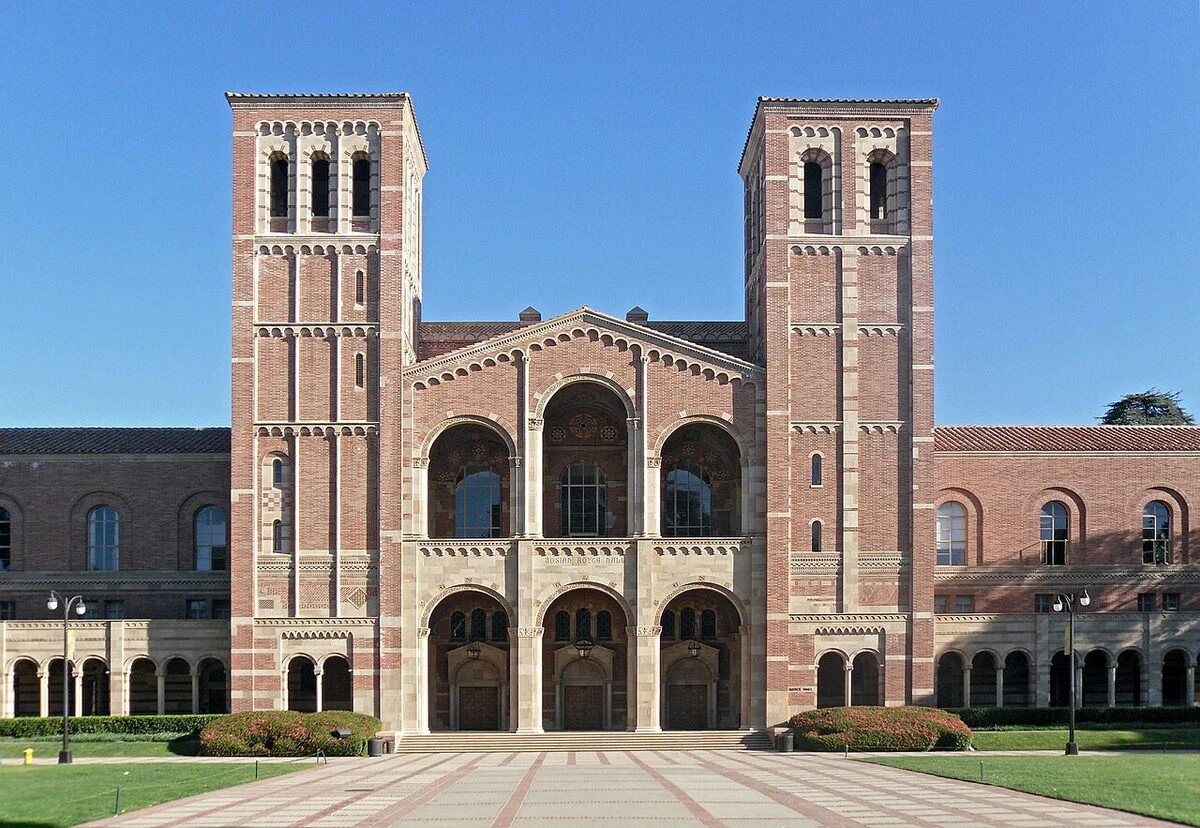 Royce Hall's red brick facade with its two arched bell towers and triple-arched entrance under a blue sky at UCLA