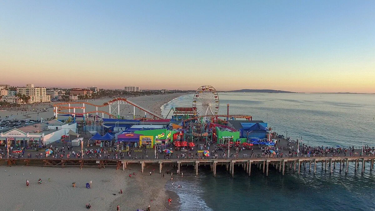 Santa Monica Pier from the air at dusk, with the Ferris wheel, the roller coaster and the pier lights on
