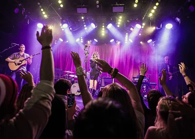 Fans with raised hands in front of the Teragram Ballroom stage as a band plays under purple and white lights