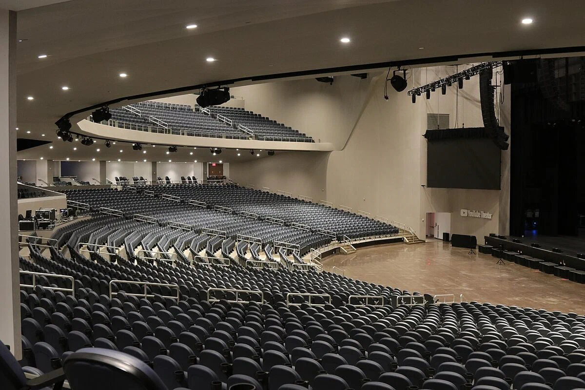 Empty tiers of dark seats curving around the stage floor inside YouTube Theater in Inglewood